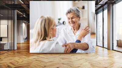 A health visitor talking to a sick senior woman sitting on bed at home. Wall mural