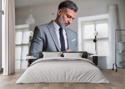 A mature businessman standing in an office, using tablet. Wall mural