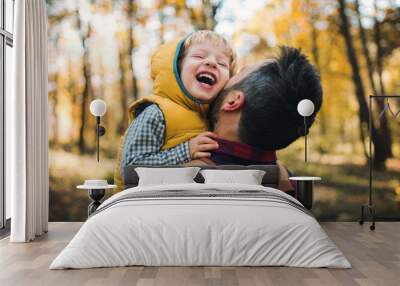 A mature father holding a toddler son in an autumn forest, having fun. Wall mural