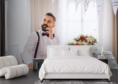 A portrait of a thoughtful mature man sitting indoors in a room set for a party. Wall mural