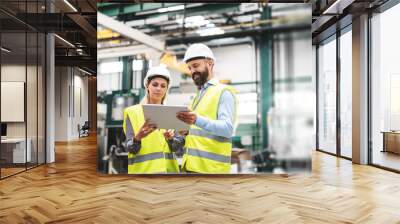 A portrait of an industrial man and woman engineer with tablet in a factory, talking. Wall mural