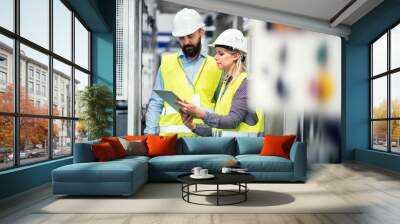 A portrait of an industrial man and woman engineer with tablet in a factory, talking. Wall mural