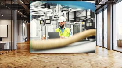 A portrait of an industrial man engineer with laptop in a factory, working. Wall mural