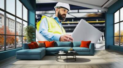 A portrait of an industrial man engineer with laptop in a factory, working. Wall mural