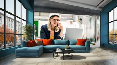 A portrait of an industrial woman engineer in a factory using laptop and smartphone. Wall mural