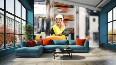 A portrait of an industrial woman engineer on the phone, standing in a factory. Wall mural