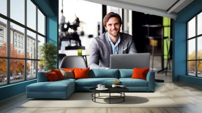 A portrait of young businessman with computer in an office, looking at camera. Wall mural