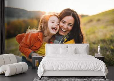 A portrait of young mother with a small daughter in autumn nature at sunset. Wall mural