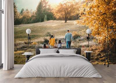 A rear view of young family with two small children walking in autumn nature. Wall mural