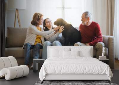 A senior couple with a teenage girl sitting on a sofa with dog at home. Wall mural