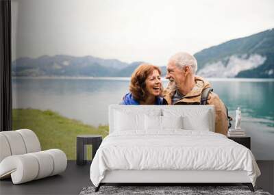 A senior pensioner couple walking by lake in nature, talking. Wall mural