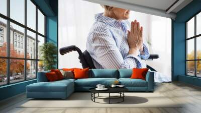 A senior woman in wheelchair praying at home. Wall mural