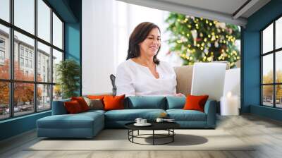 A senior woman with laptop sitting on a sofa at home at Christmas time. Wall mural