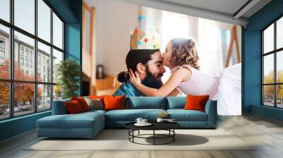 A side view of small girl with a princess crown and young father at home, playing. Wall mural