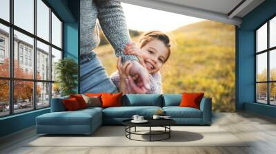 A small girl with unrecognizable father in autumn nature, having fun. Wall mural