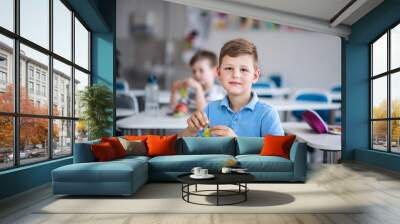 A small school boy sitting at the desk in classroom, eating grapes. Wall mural