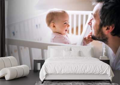 A small toddler girl standing in cot with her father at home. Wall mural