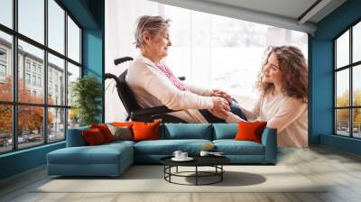 A teenage girl with grandmother at home, holding hands. Wall mural