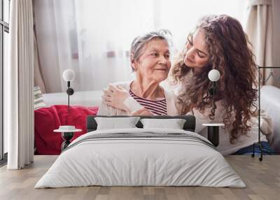 A teenage girl with grandmother at home, hugging. Wall mural