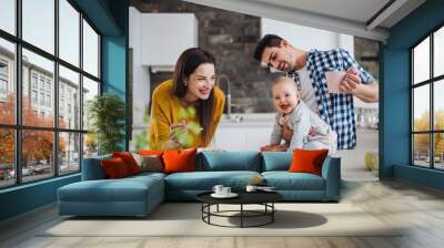 A young family at home, a man holding a baby and a woman feeding her. Wall mural