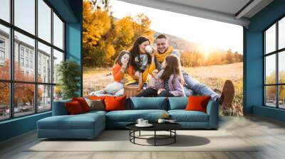 A young family with two small children having picnic in autumn nature at sunset. Wall mural