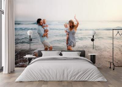 A young family with two toddler children having fun on beach on summer holiday. Wall mural