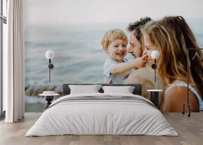 A young family with two toddler children standing on beach on summer holiday. Wall mural