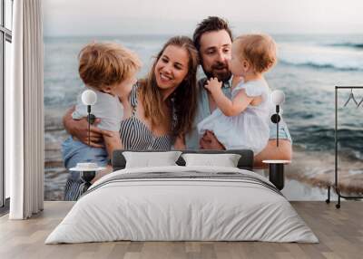 A young family with two toddler children standing on beach on summer holiday. Wall mural