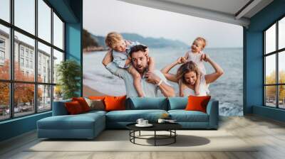 A young family with two toddler children standing on beach on summer holiday. Wall mural