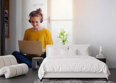 A young female student sitting at the table, using headphones when studying. Wall mural