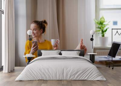 A young female student sitting at the table, using smartpone when studying. Wall mural