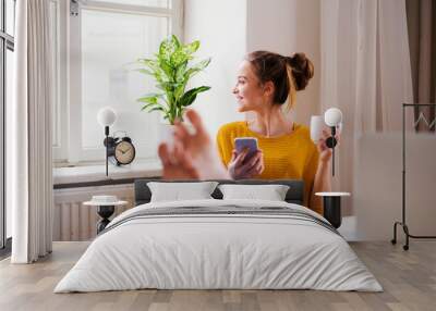 A young female student sitting at the table, using smartpone when studying. Wall mural