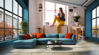 A young female student sitting on window sill, using tablet when studying. Wall mural