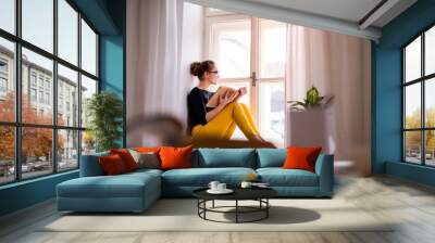 A young female student with a book sitting on window sill, studying. Wall mural