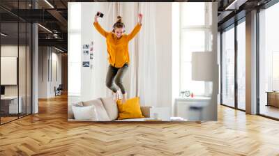 A young female student with headphones jumping on sofa when studying. Wall mural