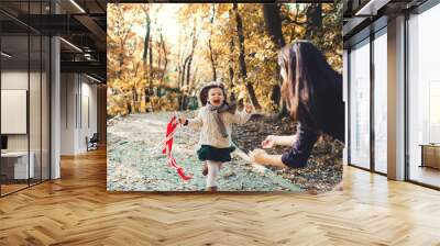 A young mother with a toddler daughter running in forest in autumn nature. Wall mural