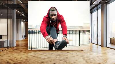 A young sporty black man runner tying shoelaces outside in a city. Wall mural