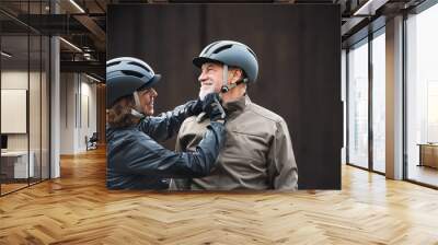 Active senior couple with bike helmets standing outdoors againts dark background. Wall mural