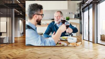 An adult hipster son and senior father indoors at home, eating light lunch. Wall mural