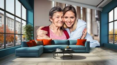 An elderly grandmother with an adult granddaughter at home, hugging. Wall mural