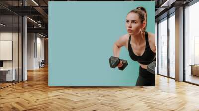 Athletic fitness woman working out with dumbbells on green background. Copy space. Wall mural