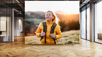 Attractive senior woman walking outdoors in nature at sunset, hiking. Wall mural