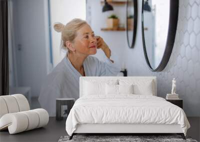 Beautiful senior woman in bathrobe applying natural face cream in bathroom, skin care and morning routine concept. Wall mural