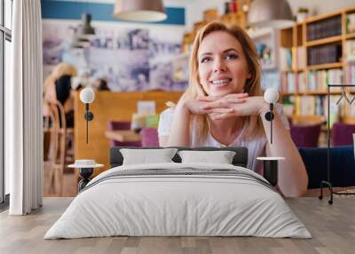 blond woman sitting in modern city cafe smiling Wall mural