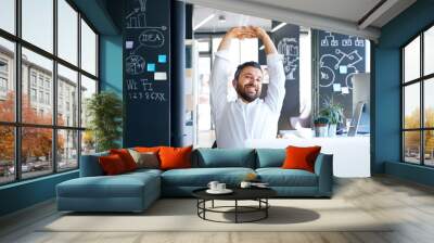 Businessman at the desk in his office stretching arms. Wall mural