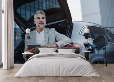 Businessman using tablet while charging car at electric vehicle charging station, closeup. Wall mural