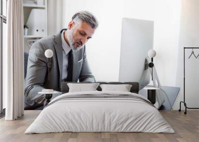 Businessman with computer sitting at the table in an office, making notes. Wall mural