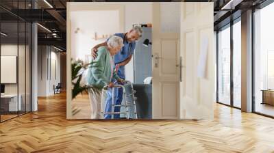 Caregiver helping senior woman to walk in her home with walker. Wall mural