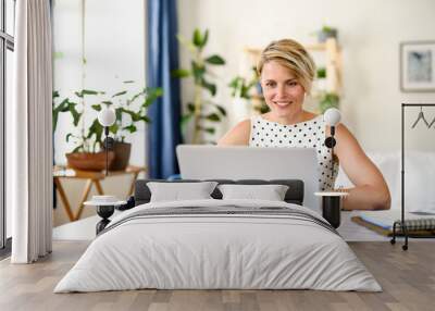 Cheerful young businesswoman with laptop indoors in home office, working. Wall mural