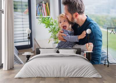 Cheerful young father with small daughter indoors in bedroom playing. Wall mural